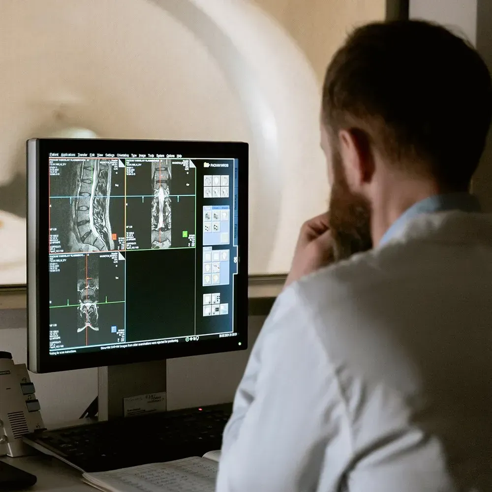 Doctor in white coat examines spinal MRI on computer screen.