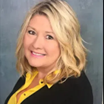 Blonde woman smiling, wearing a black top with a yellow collar.