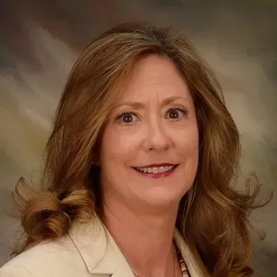 Woman with brown hair and a cream-colored blazer smiles, looking at the camera.