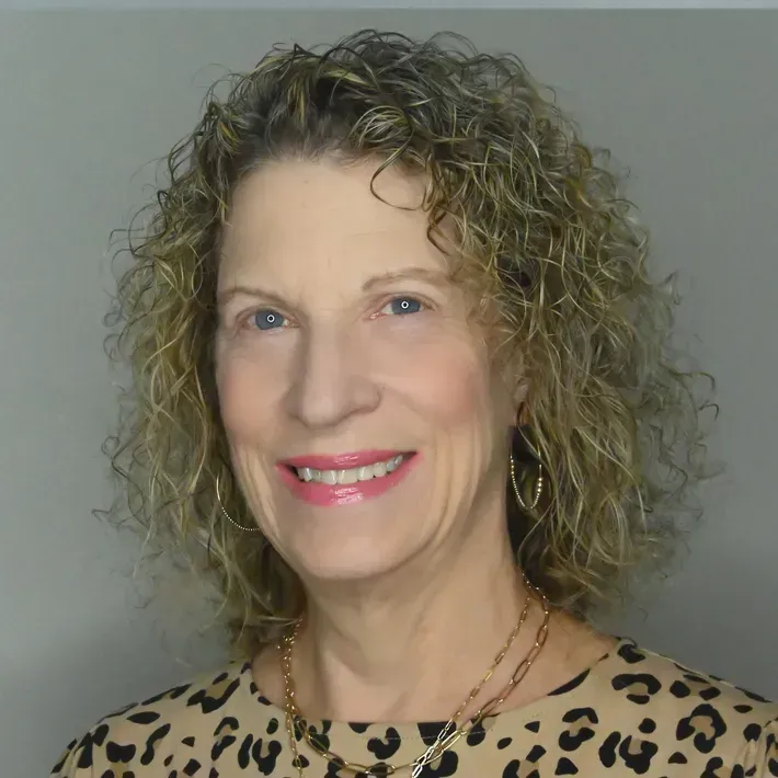 Woman with curly hair, smiling, wearing a leopard-print top and gold jewelry.