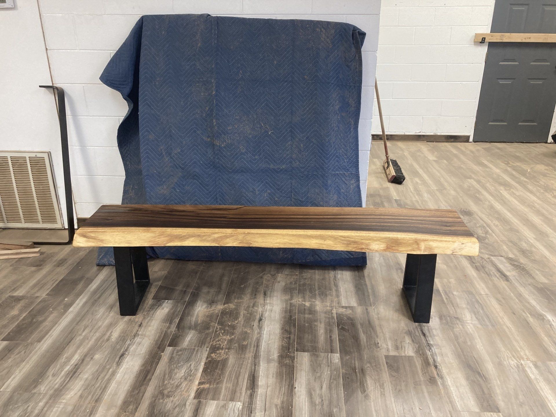 A wooden bench is sitting on a wooden floor next to a blue blanket.