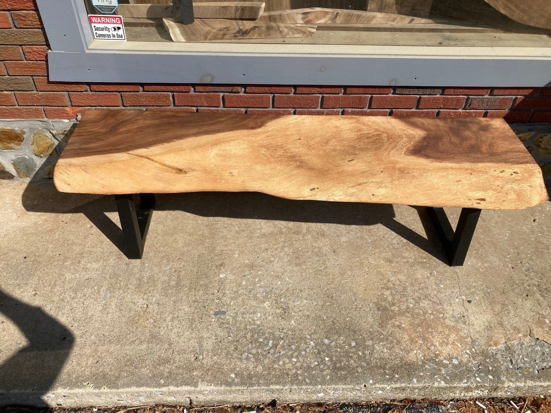 A wooden bench is sitting on a sidewalk in front of a brick building.