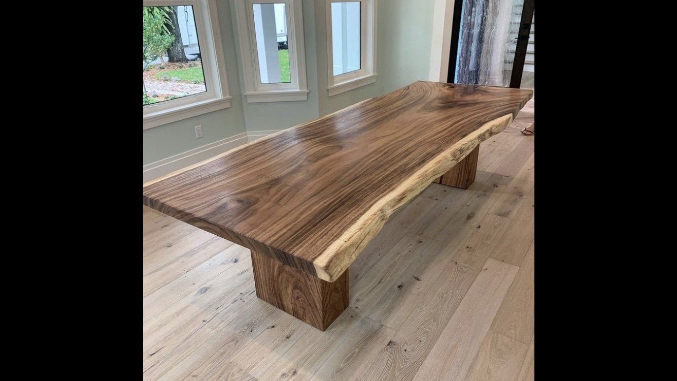 A large wooden table is sitting in a room next to a window.