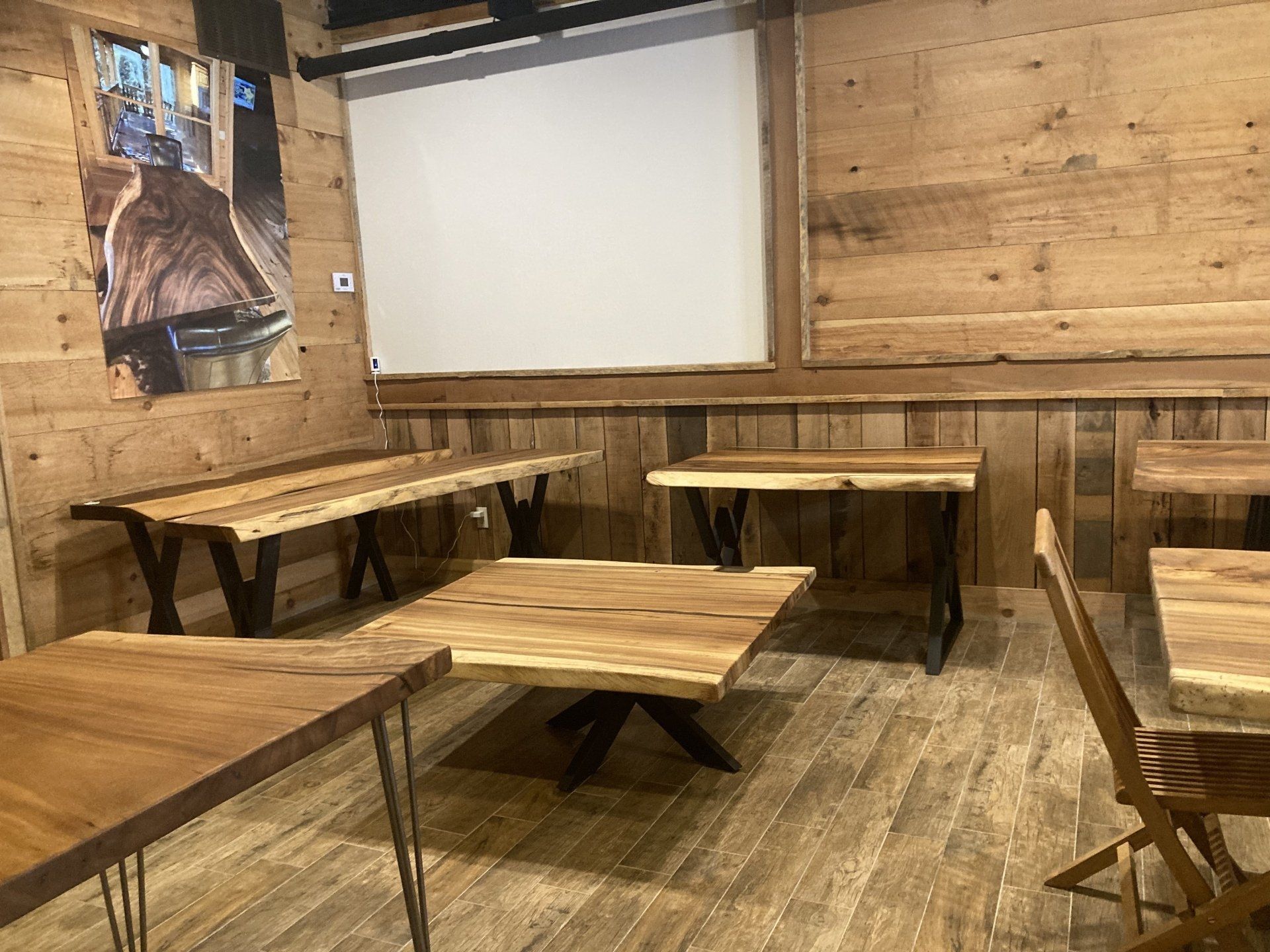 A room with wooden tables and chairs and a projector screen.