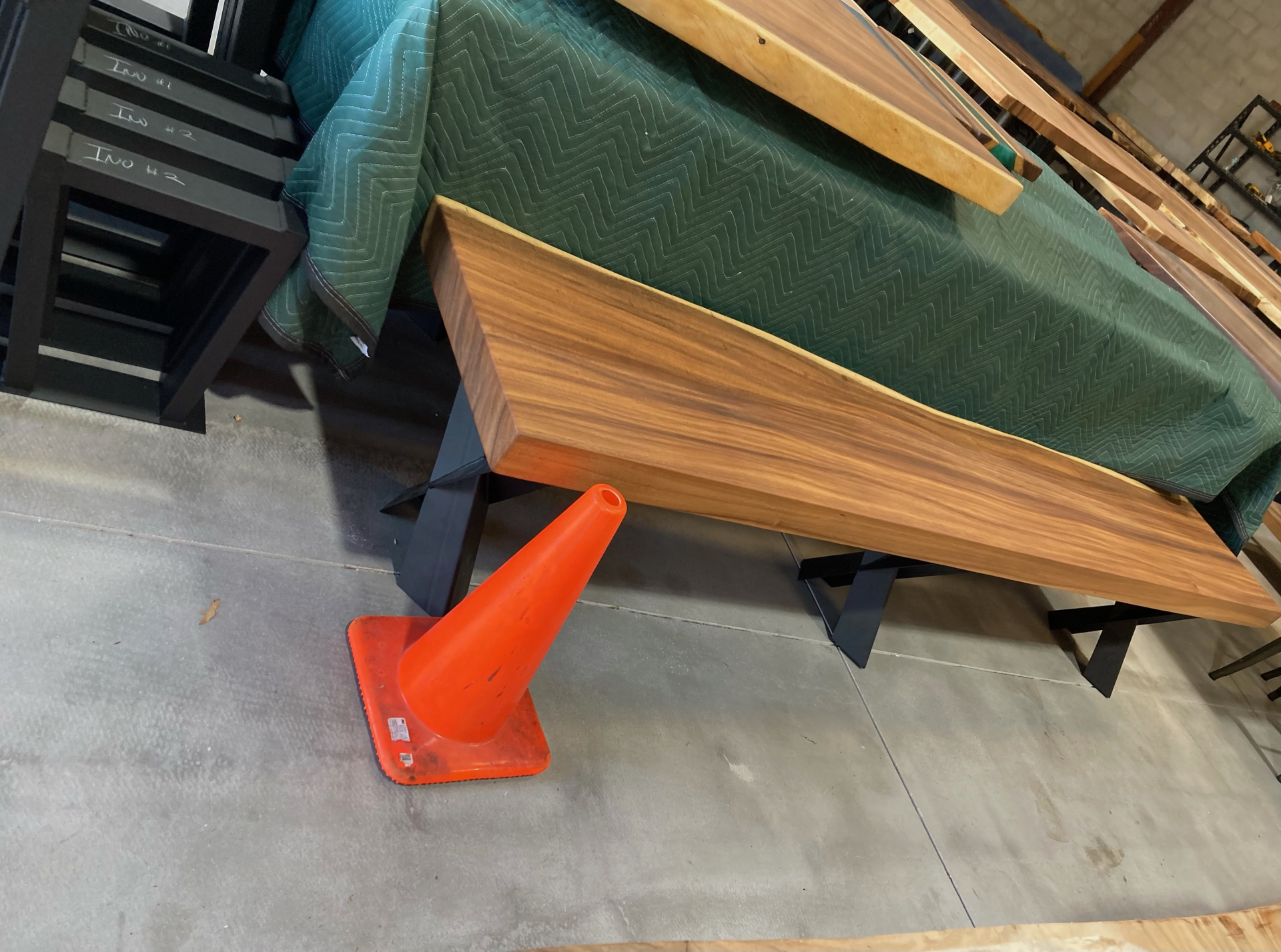 A wooden bench is sitting next to an orange traffic cone.