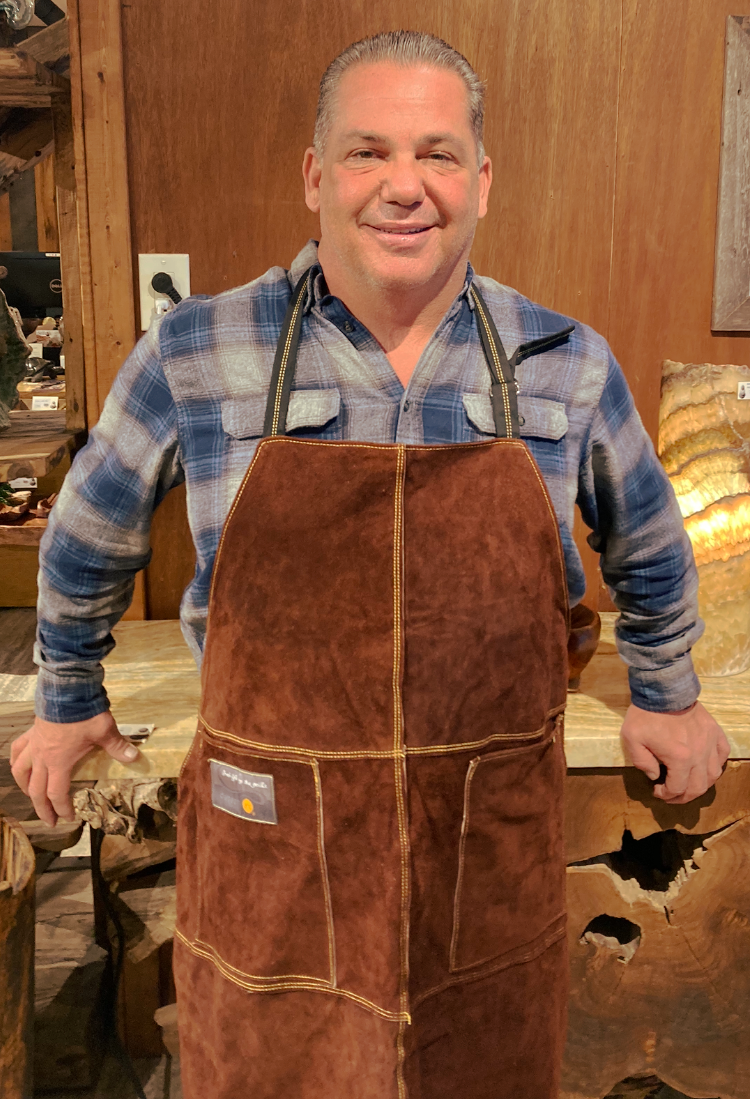 A man wearing an apron is standing in front of a wooden wall.