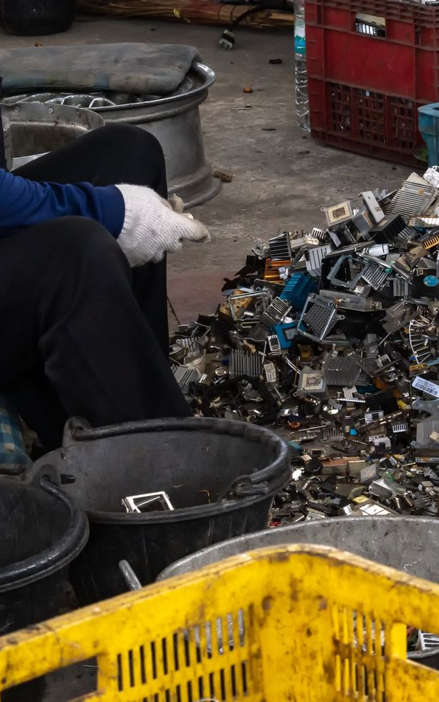 Portrait of worker with gloved hands, standing in front of scrap in a metal recycling facility.