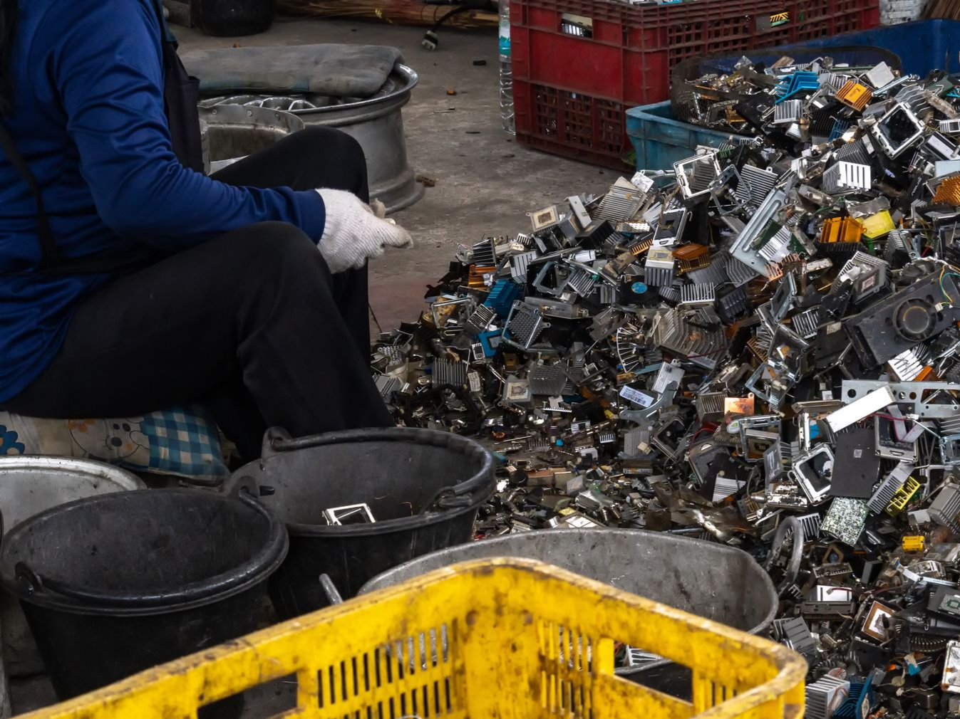 Portrait of worker with gloved hands, standing in front of scrap in a metal recycling facility.