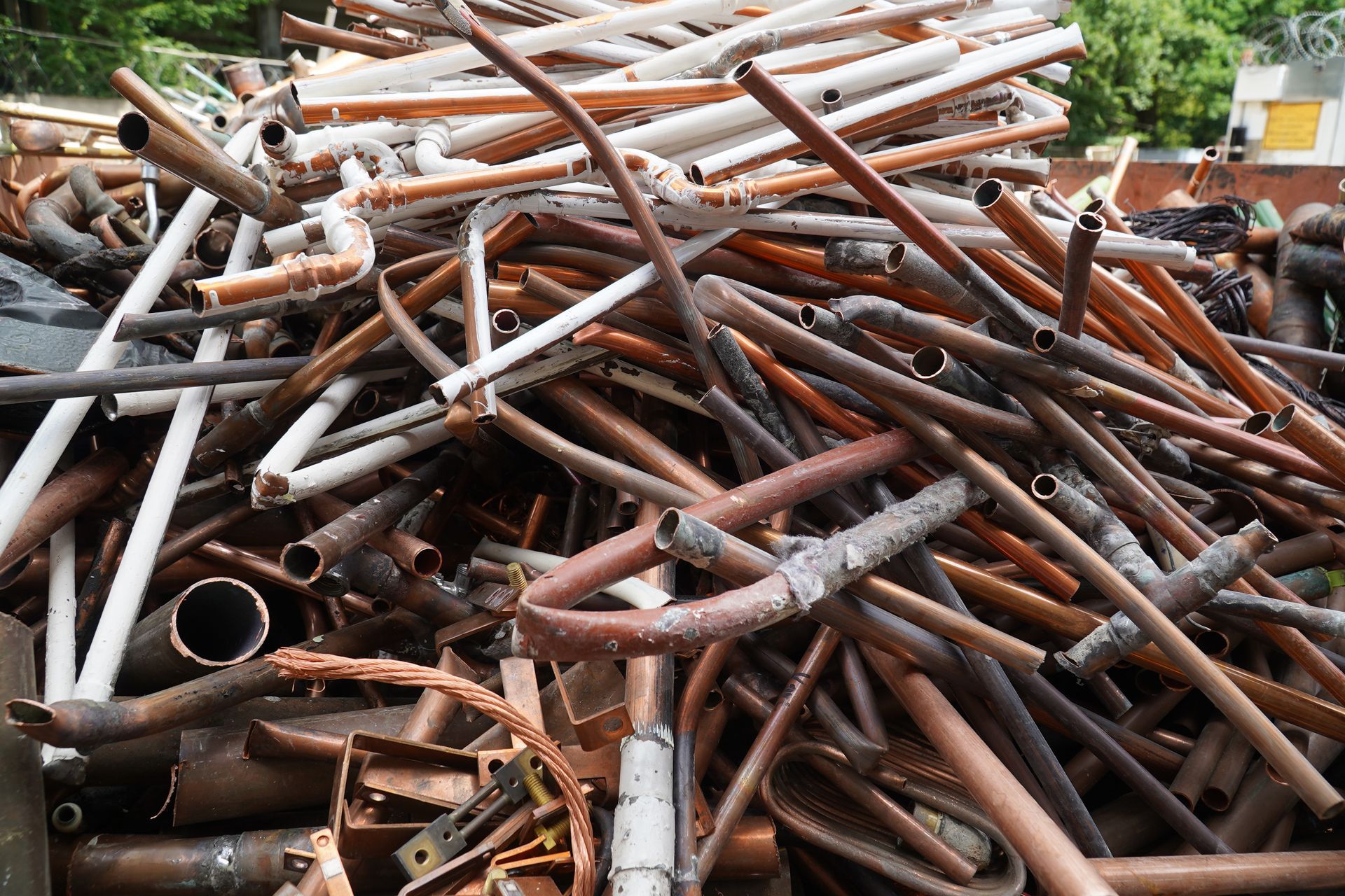Mixed non‑ferrous scrap pipes gathered in a yard, showing varied metals and wear.