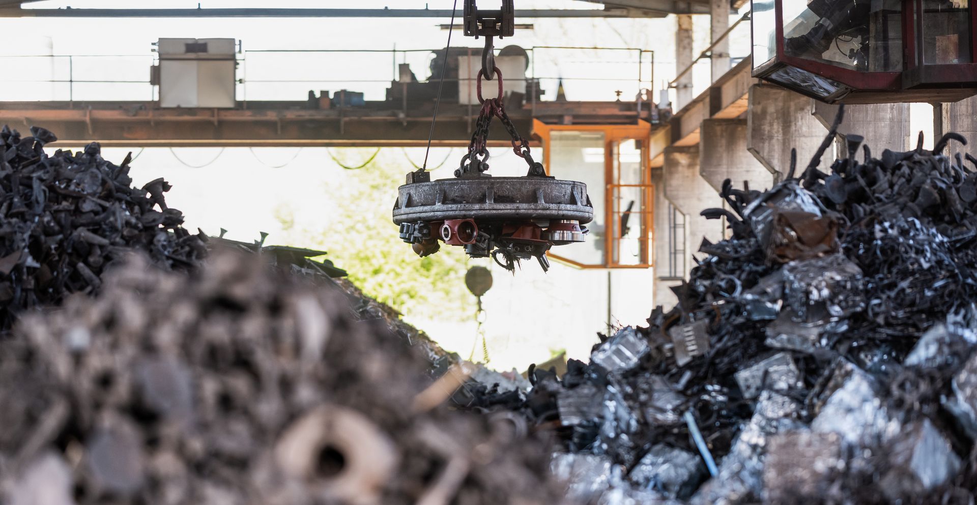 An industrial magnet lifts scrap metal at a recycling facility with large piles of metal debris. An industrial magnet lifts scrap metal at a recycling facility with large piles of metal debris.