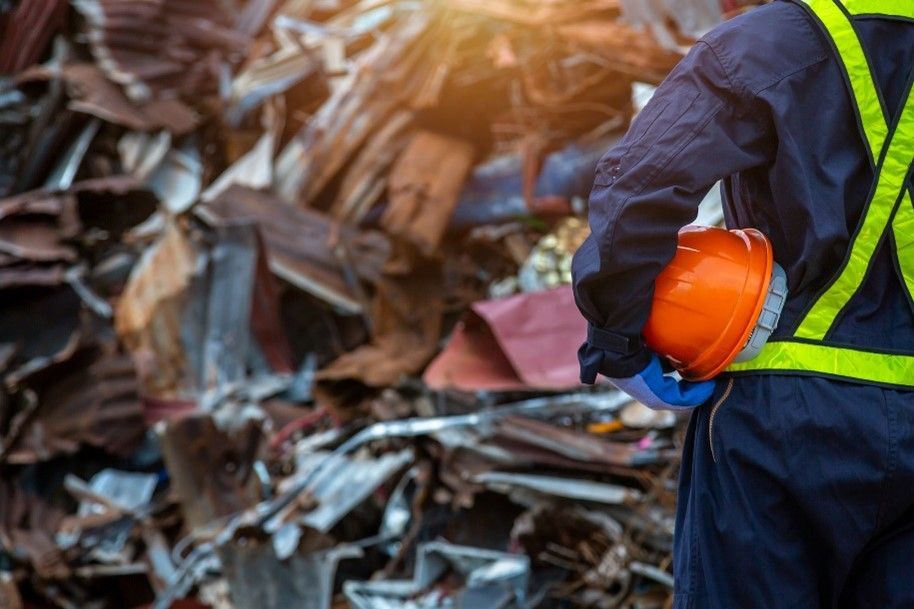 A man in a hard hat and safety vest stands by a large pile of scrap metal, promoting steel recycling.