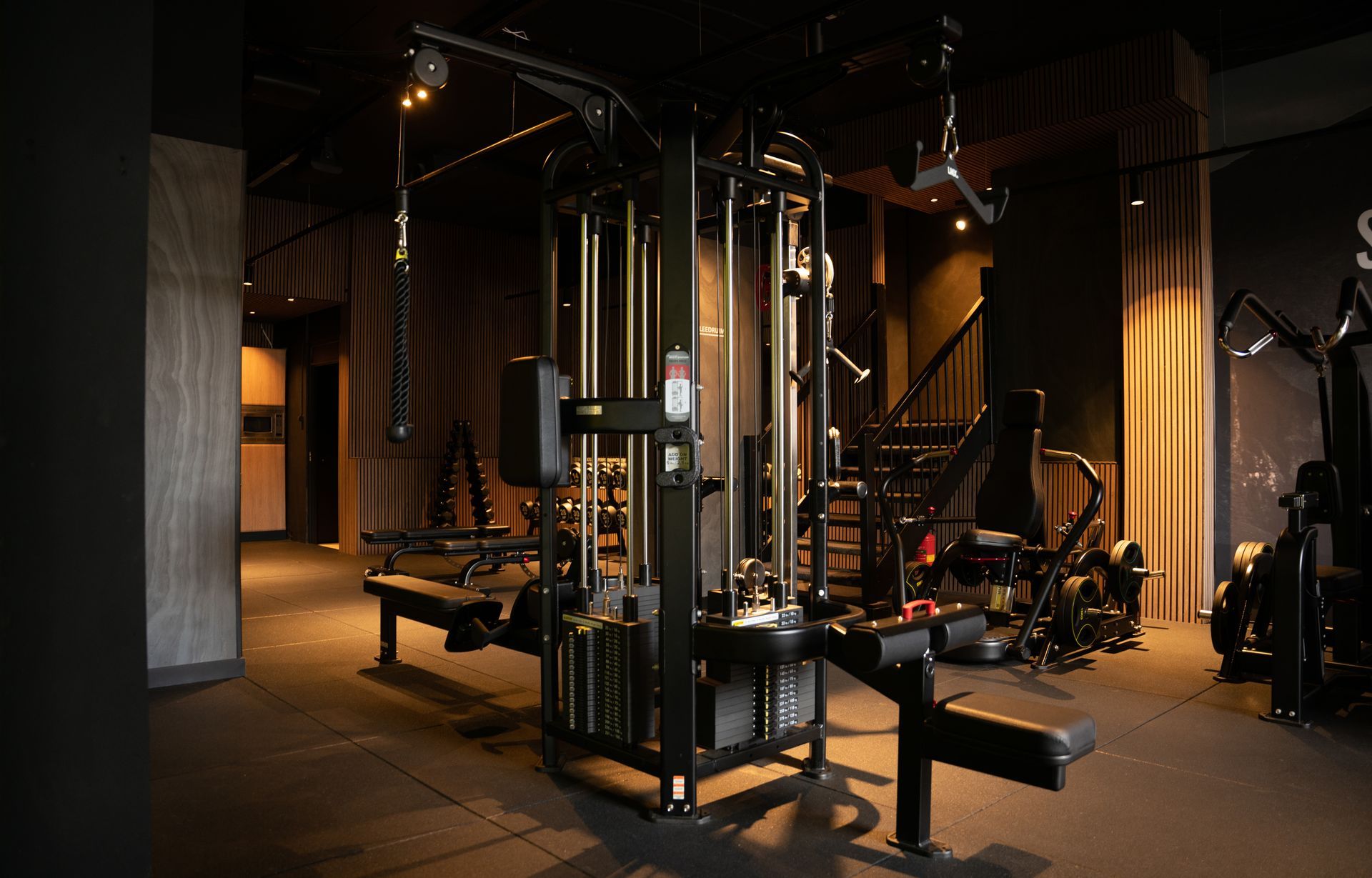 Gewichtsmachine in een sportschool met zwarte vloer en ramen, houten balken aan het plafond.