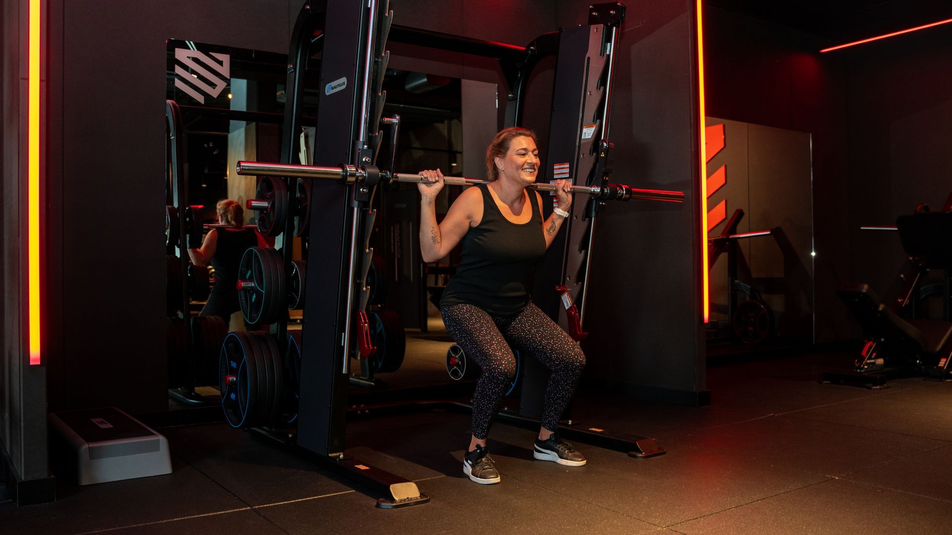 Man doet bankdrukken met spotter in de sportschool.