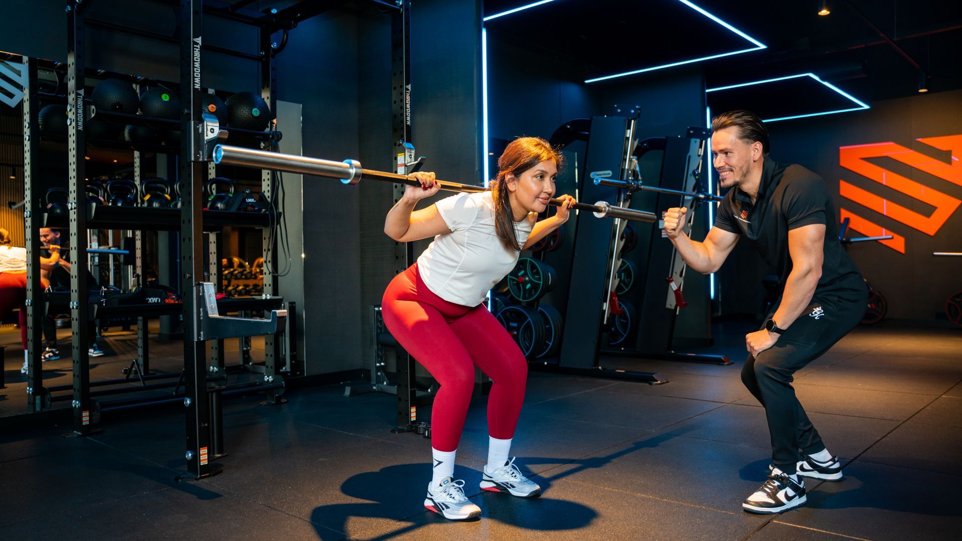 Vrouw in de sportschool met halters, kijkend in de spiegel. Zwarte sportkleding, spieren zichtbaar.