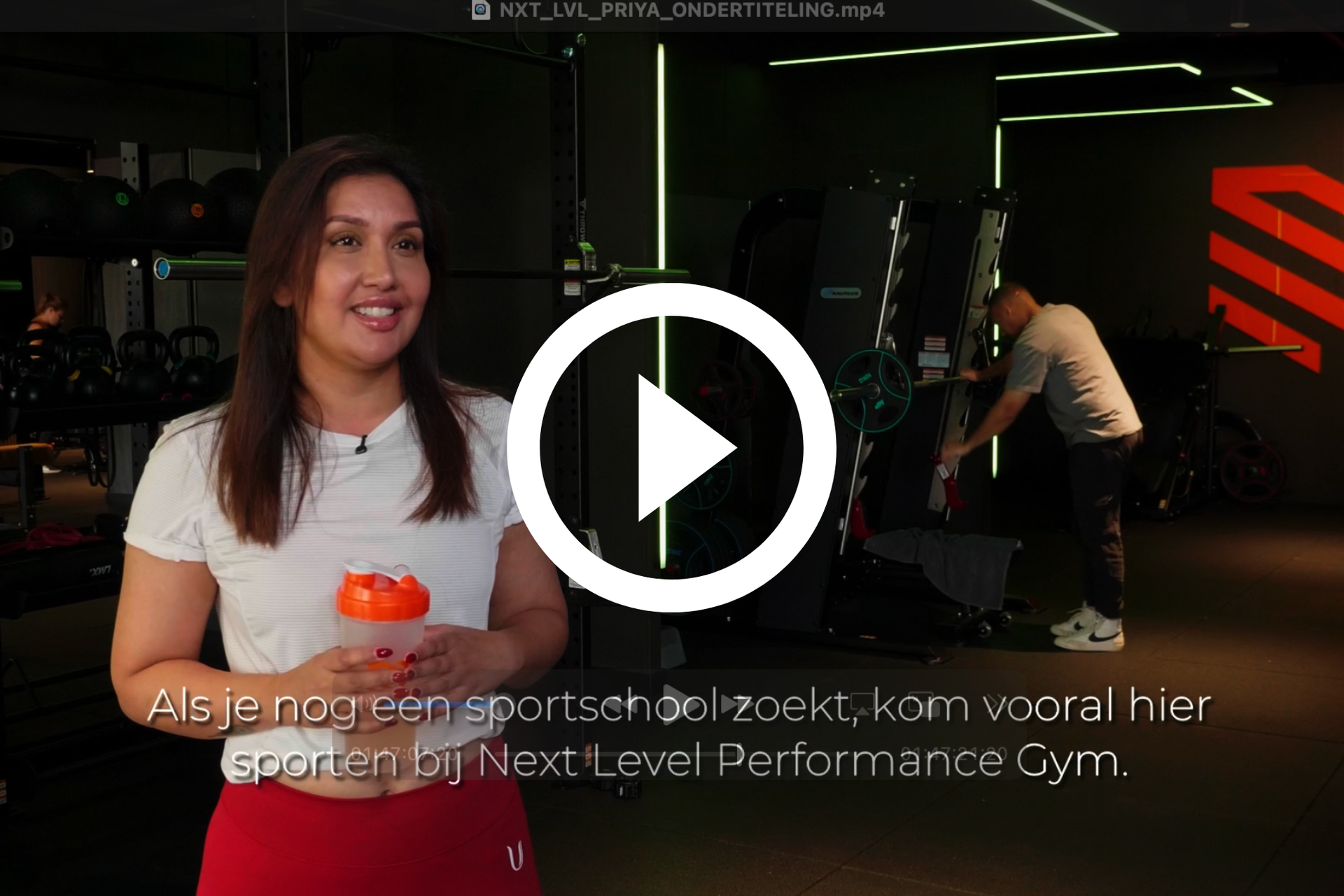 Vrouw in de sportschool met een shaker, lachend. Man op de achtergrond, fitnessapparatuur zichtbaar.