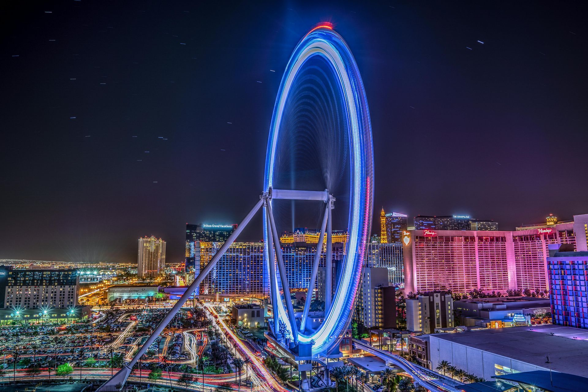 Large illuminated Ferris wheel at night, in a city. Buildings and lights in background.