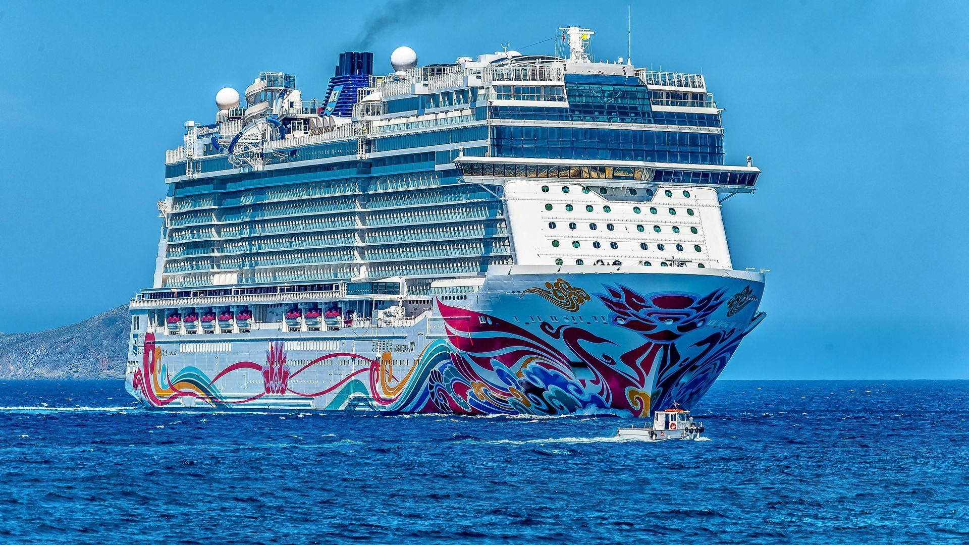 Large, colorful cruise ship on blue water; artwork on hull, smokestack emits smoke.