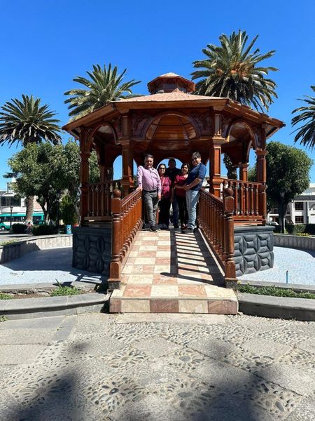 A group of people are standing in front of a wooden gazebo.