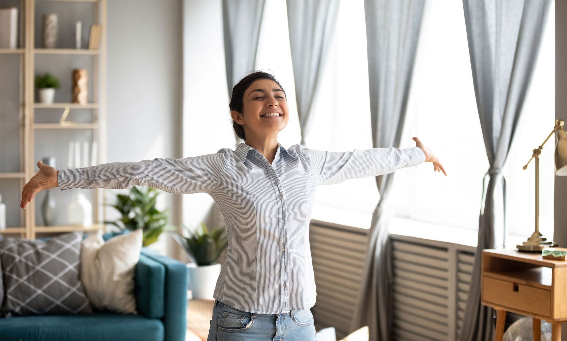 A woman is standing in a living room with her arms outstretched.