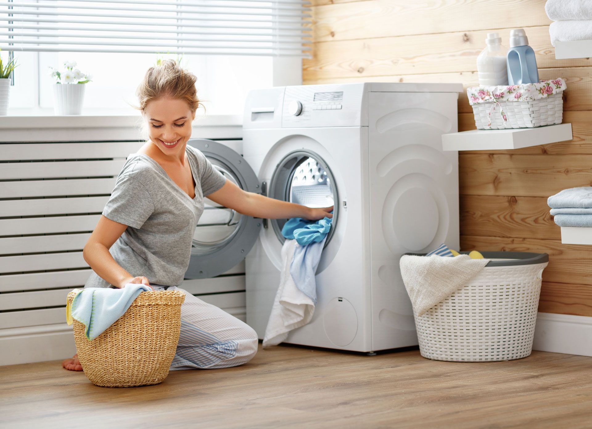 A woman is kneeling down in front of a washing machine.