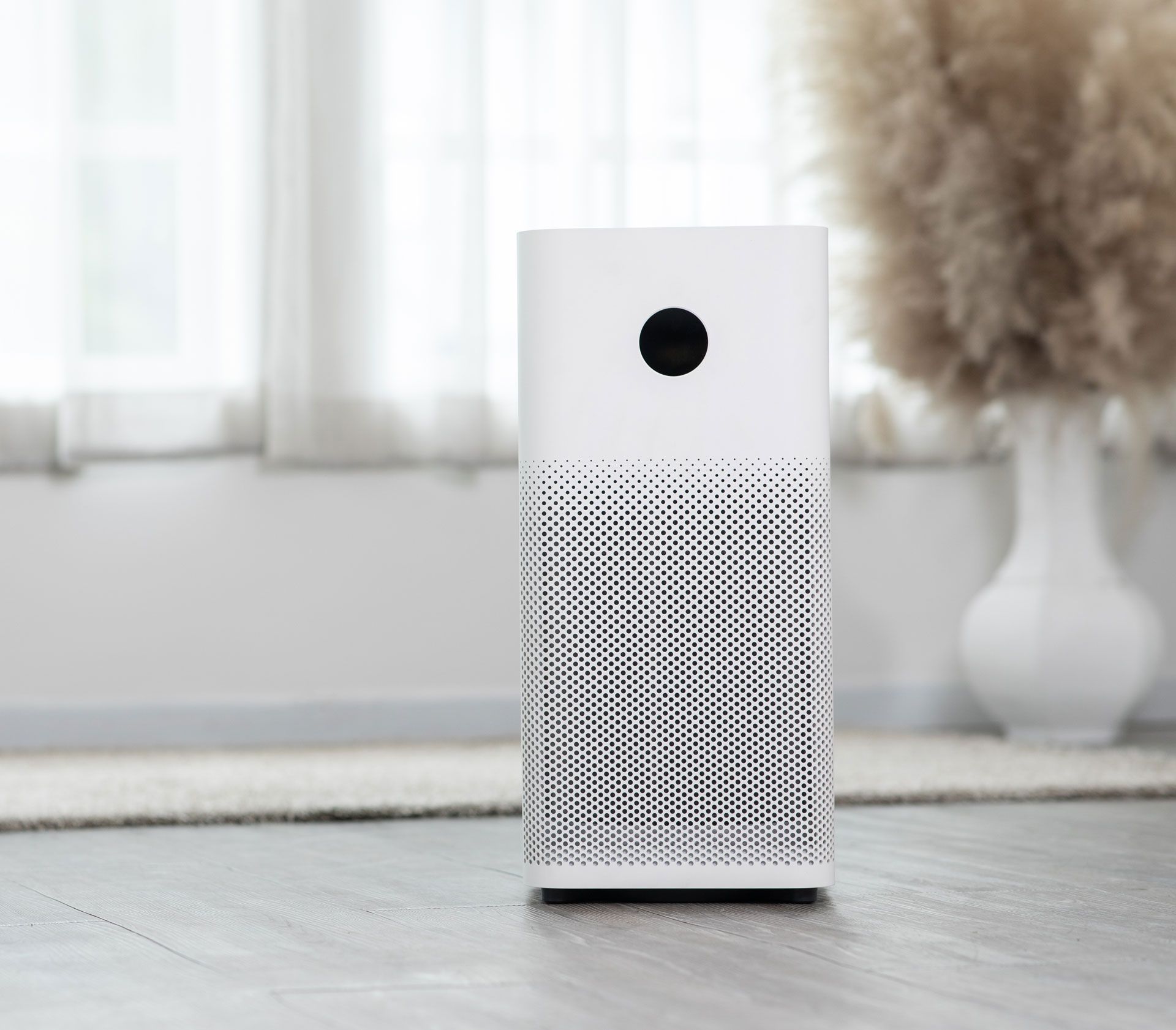 A white air purifier is sitting on the floor in front of a window.