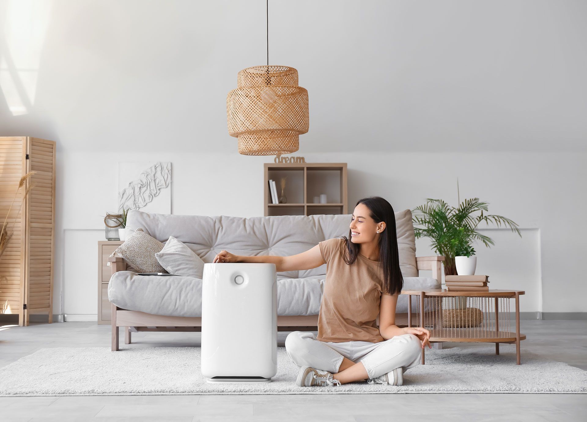 A woman is sitting on the floor in front of a air purifier in a living room.