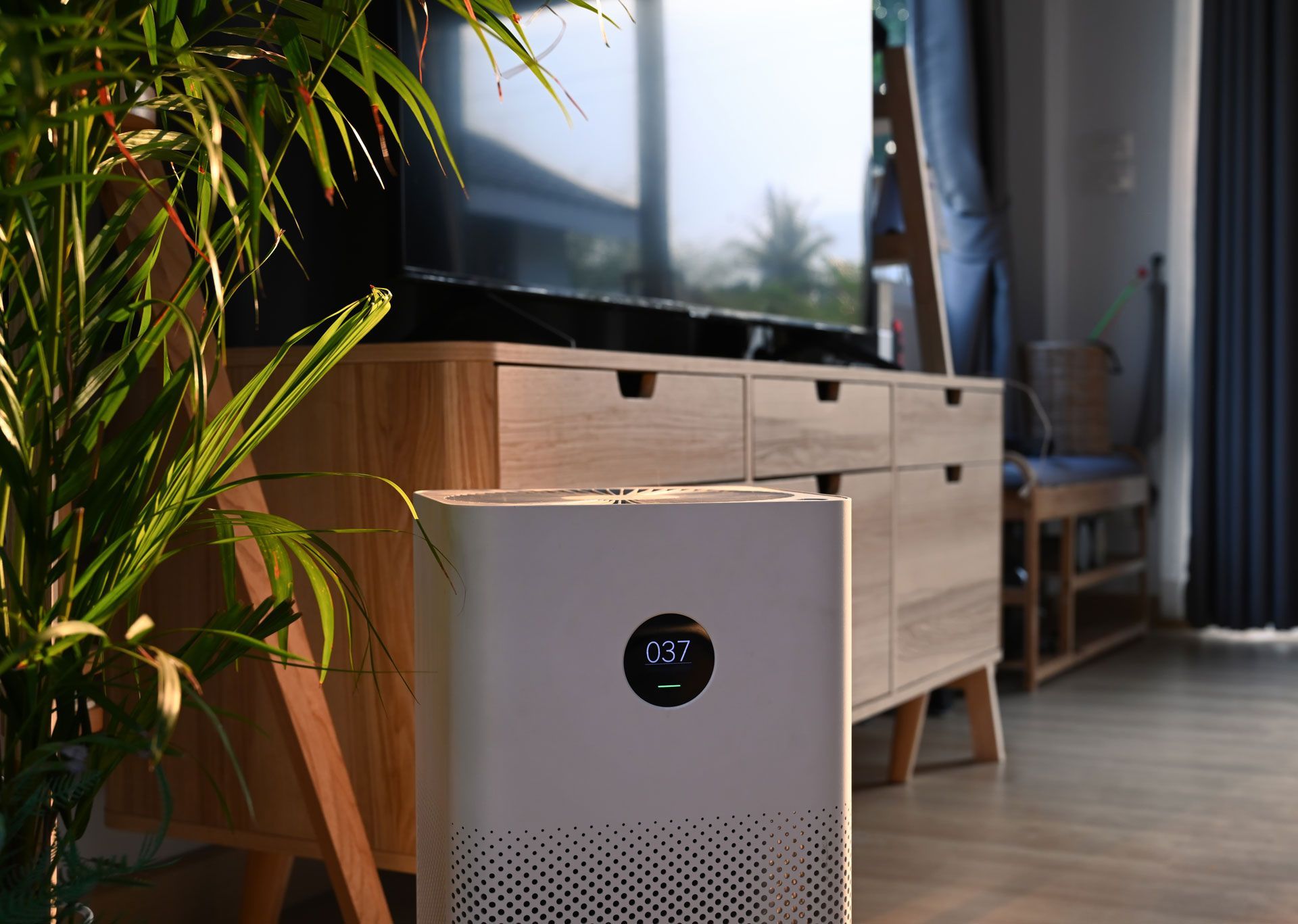 A white air purifier is sitting in a living room next to a television.