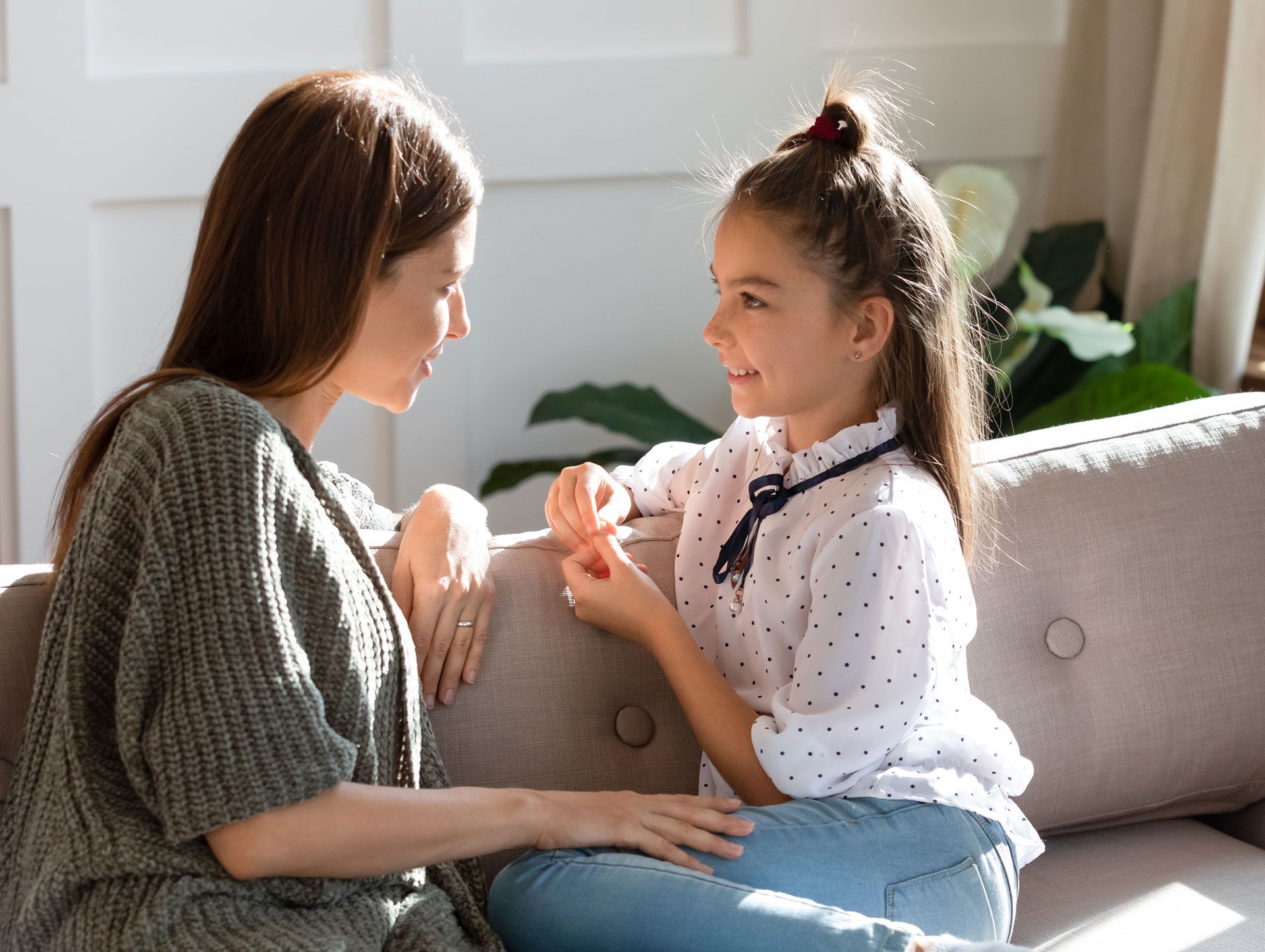 A woman and a little girl are sitting on a couch talking to each other.