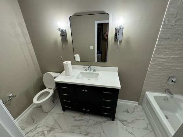 A bathroom with a toilet , sink , mirror and bathtub.