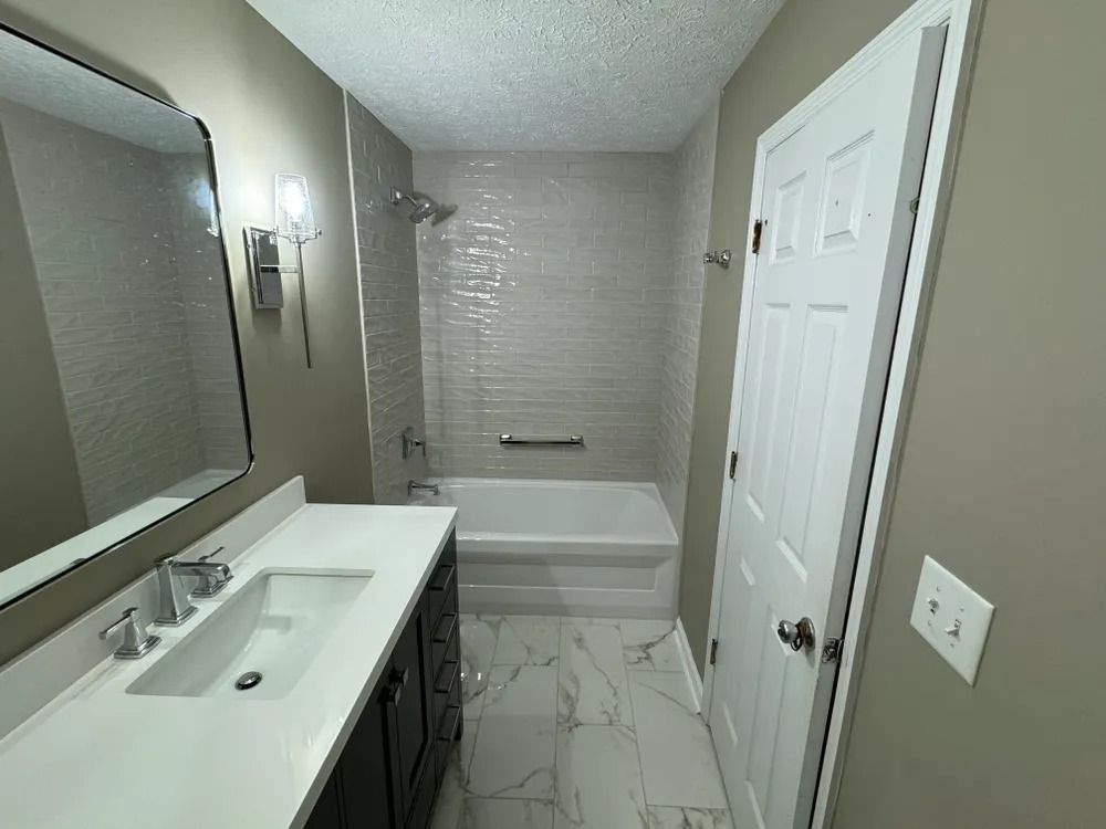 A bathroom with a sink , tub and mirror.