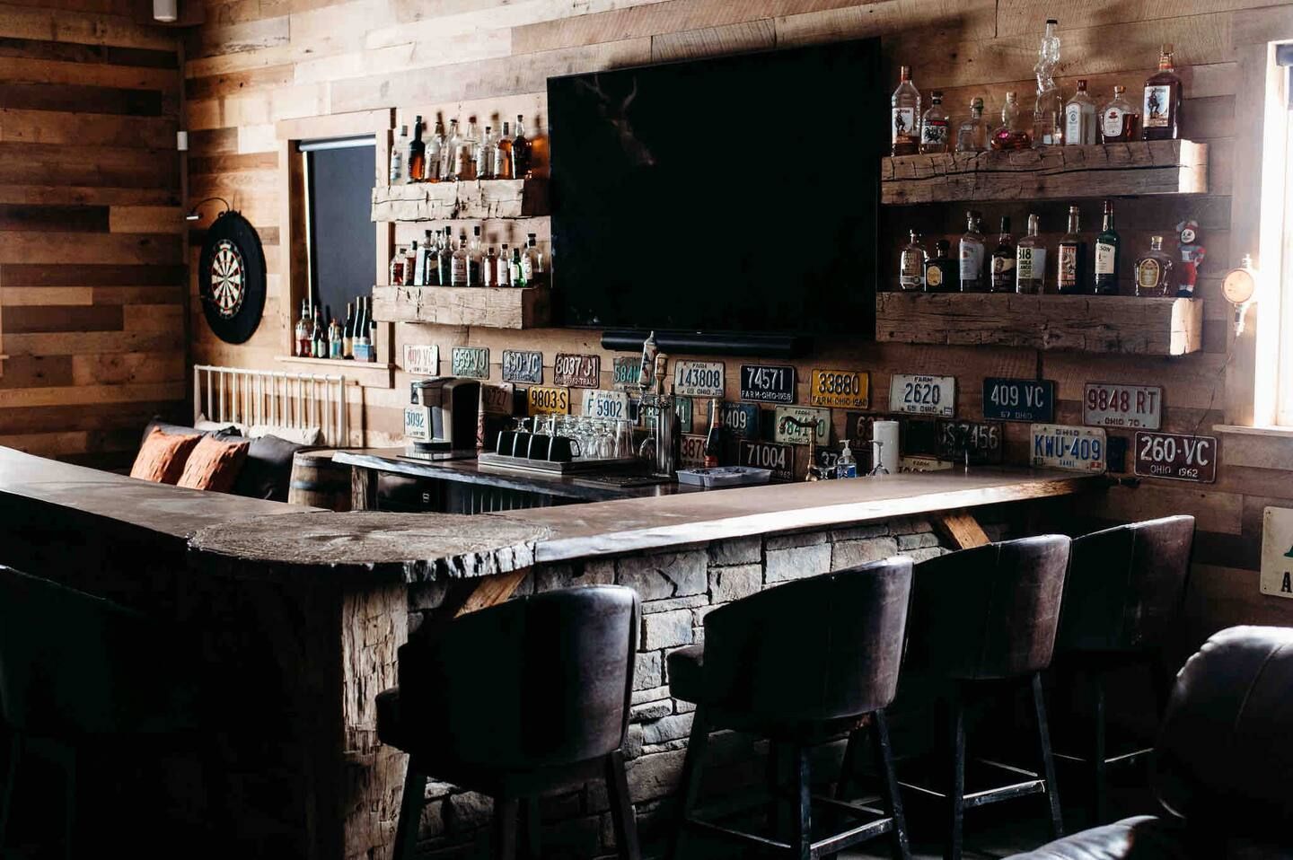 A man cave with a bar , chairs , a television , and bottles of liquor.