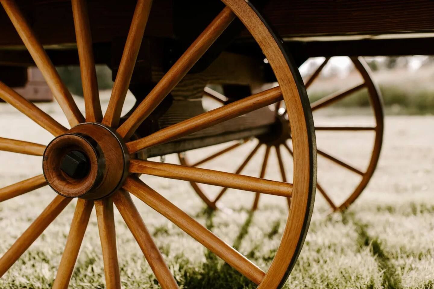 A close up of a wooden wagon wheel in a field.