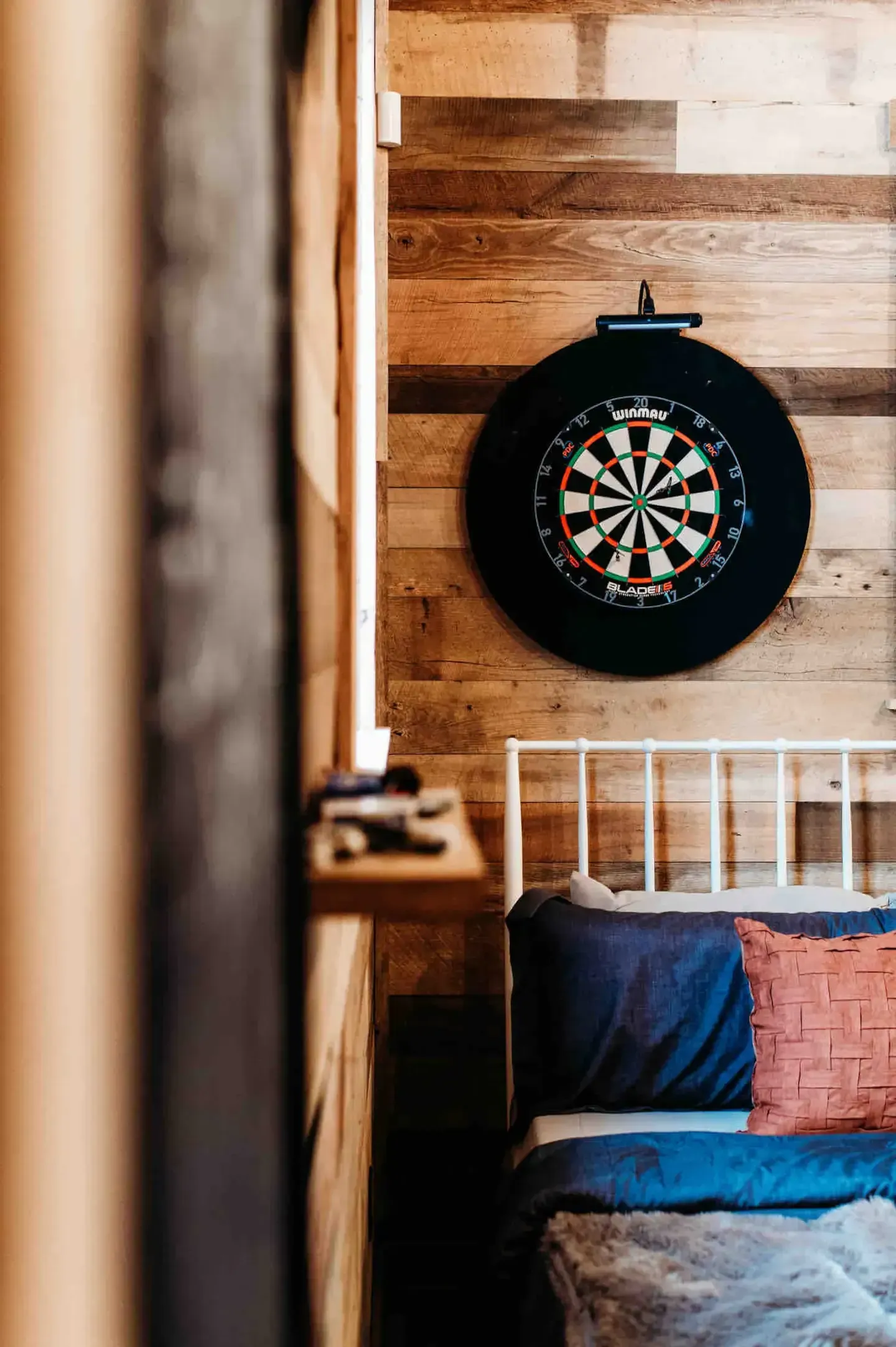 A dart board is hanging on the wall above a bed in a bedroom.