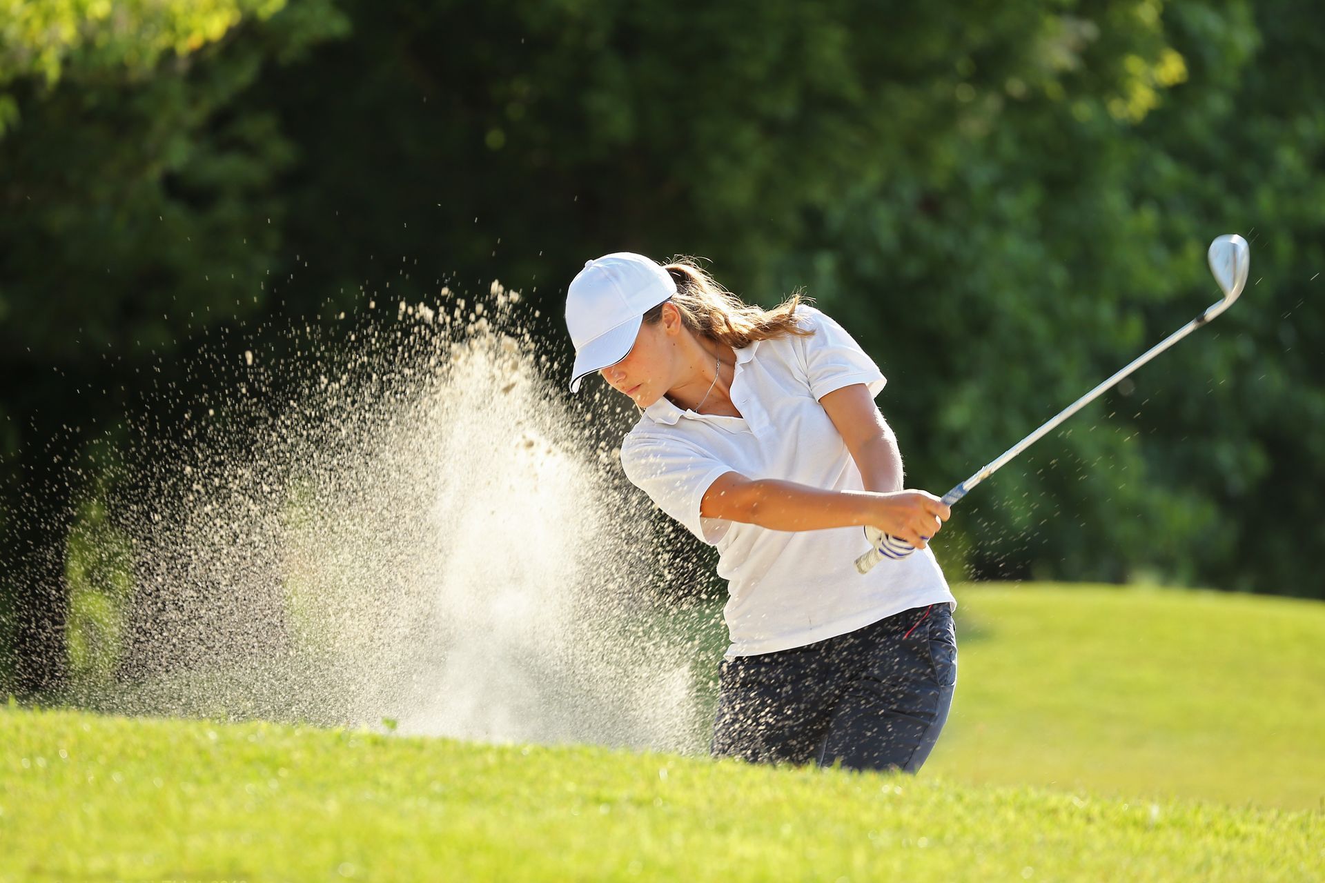 A woman is hitting a golf ball out of a bunker on a golf course.