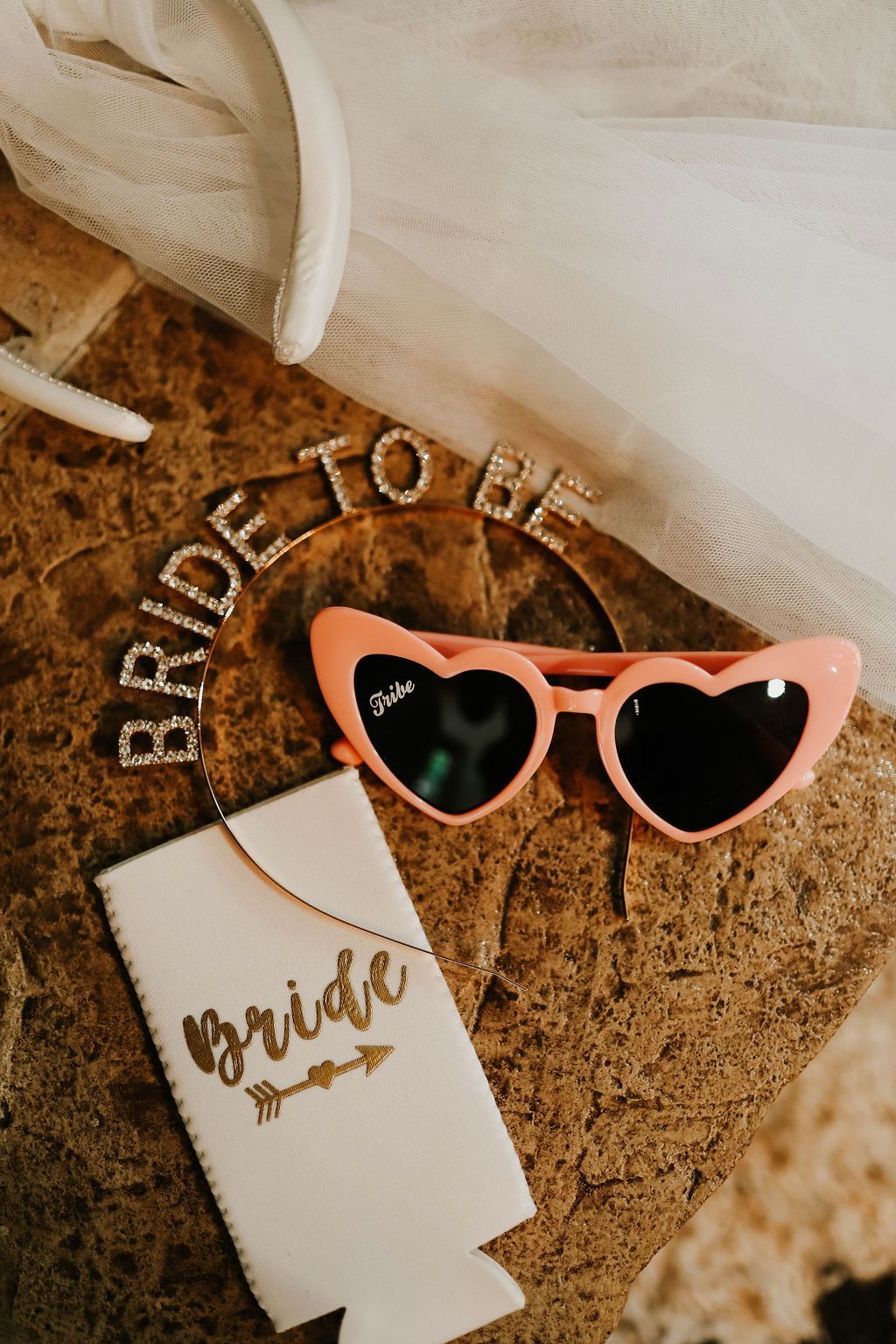 A pair of heart shaped sunglasses and a bride to be headband are on a table.