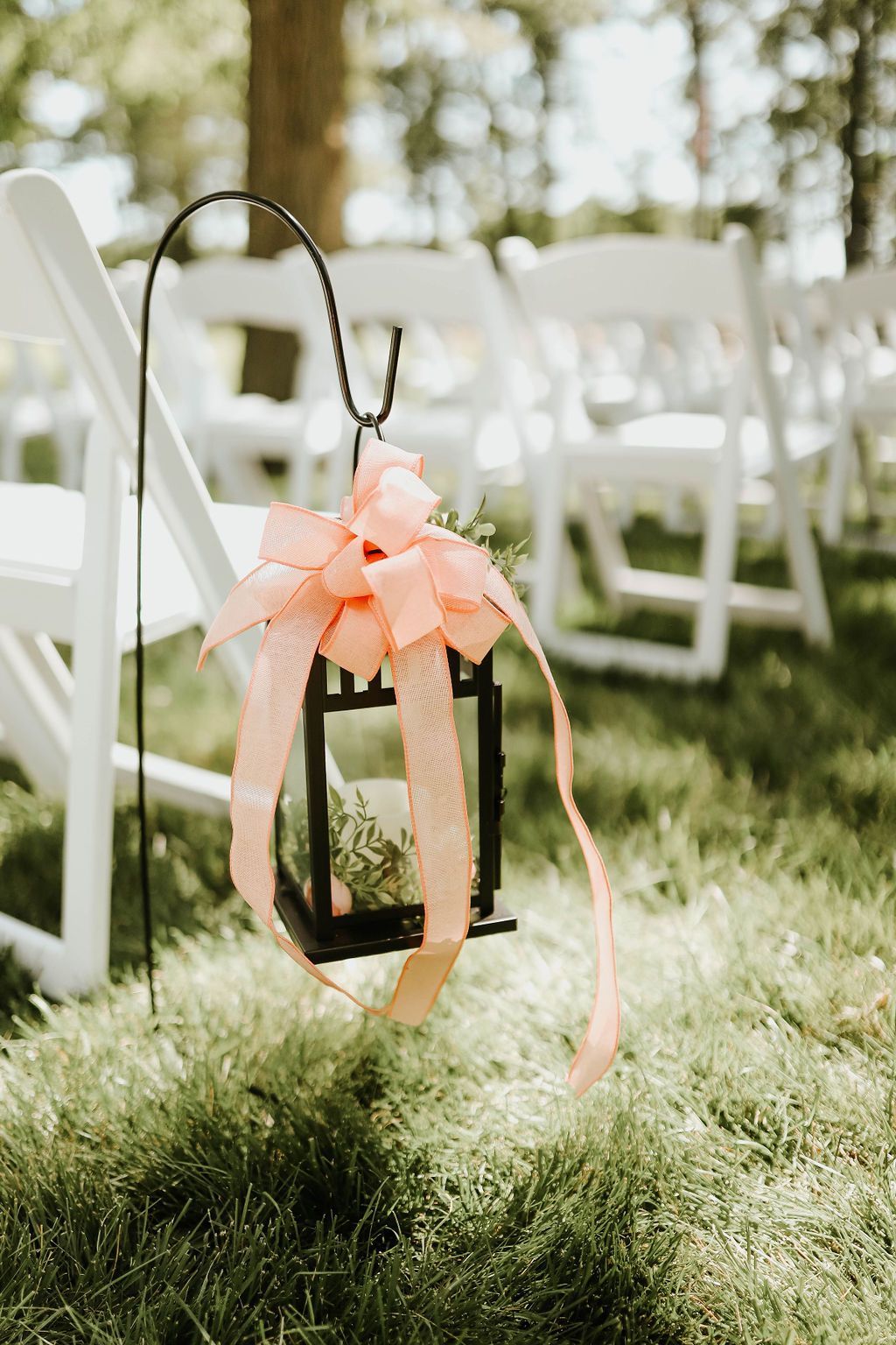 A lantern with a pink bow is sitting in the grass next to a row of white chairs.