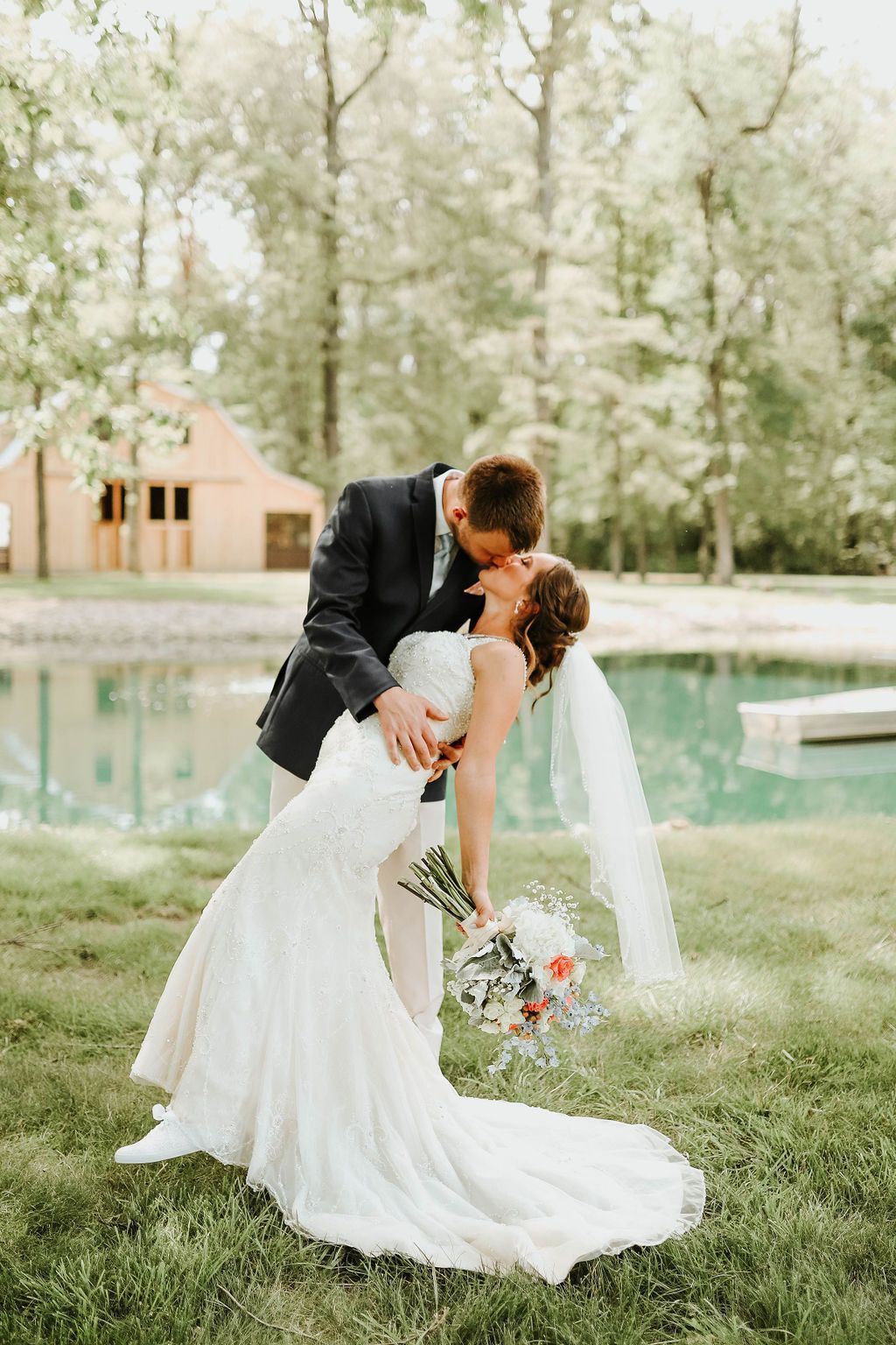 A bride and groom are kissing in front of a pool.
