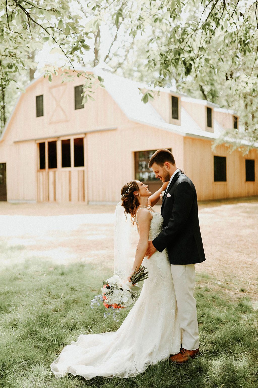 A bride and groom are kissing in front of a barn.
