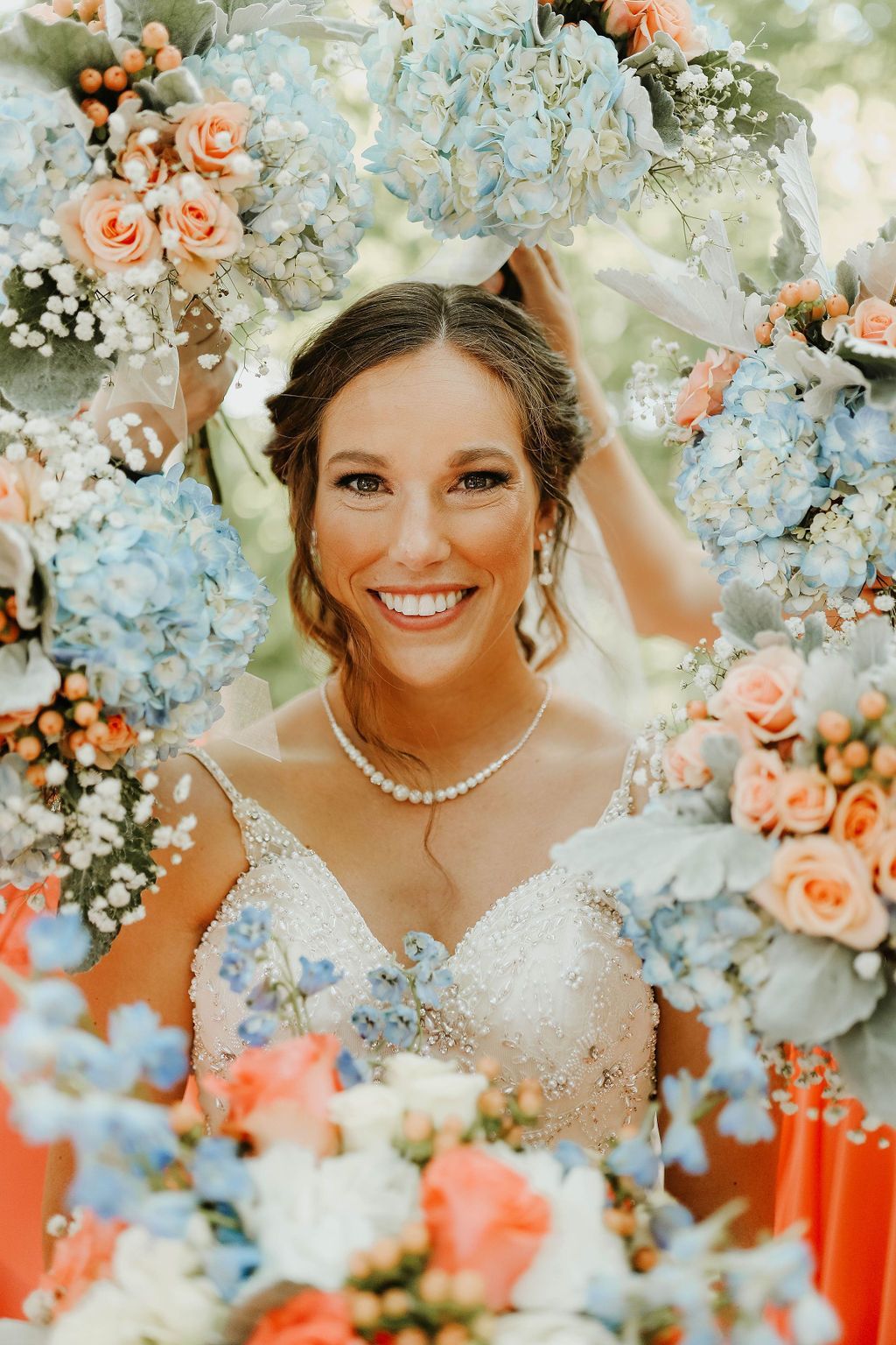 A bride in a wedding dress is surrounded by flowers and smiling.