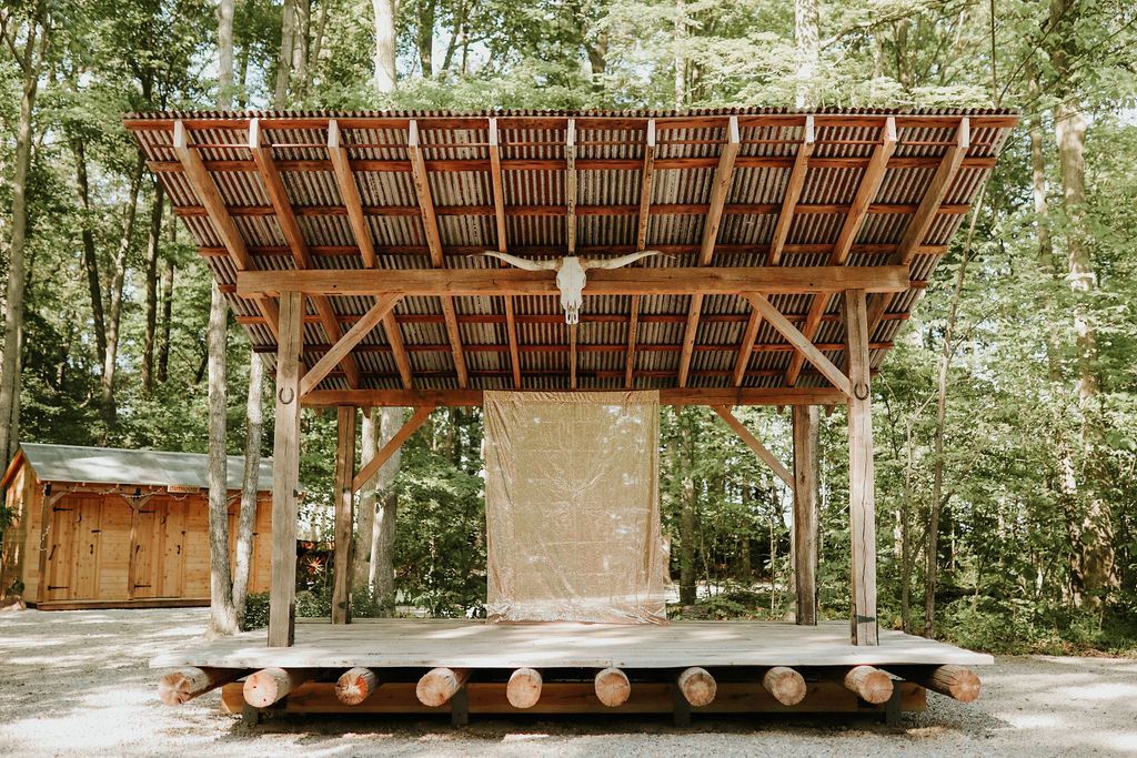 A wooden stage in the middle of a forest with a roof.