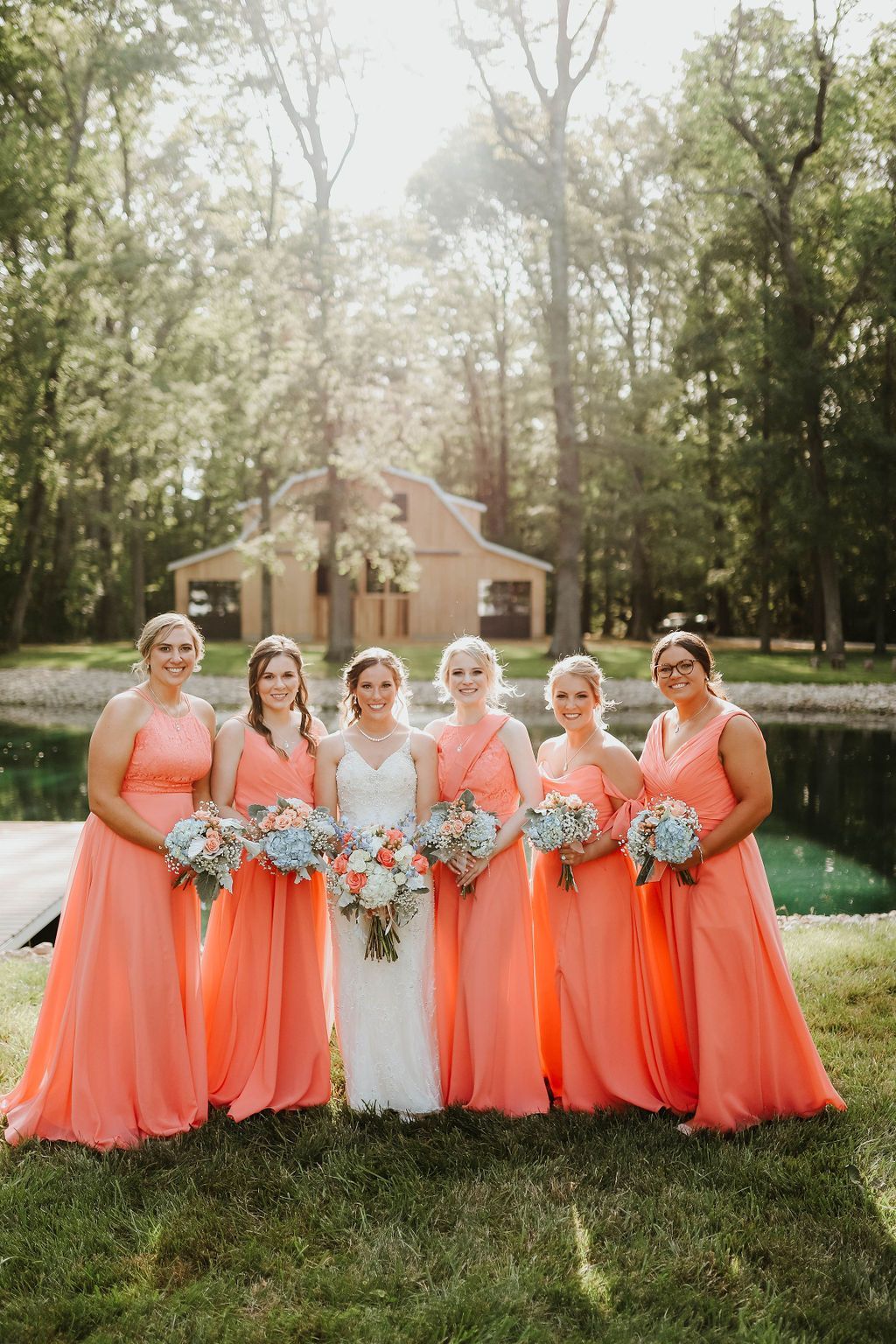 A bride and her bridesmaids are posing for a picture in front of a pond.