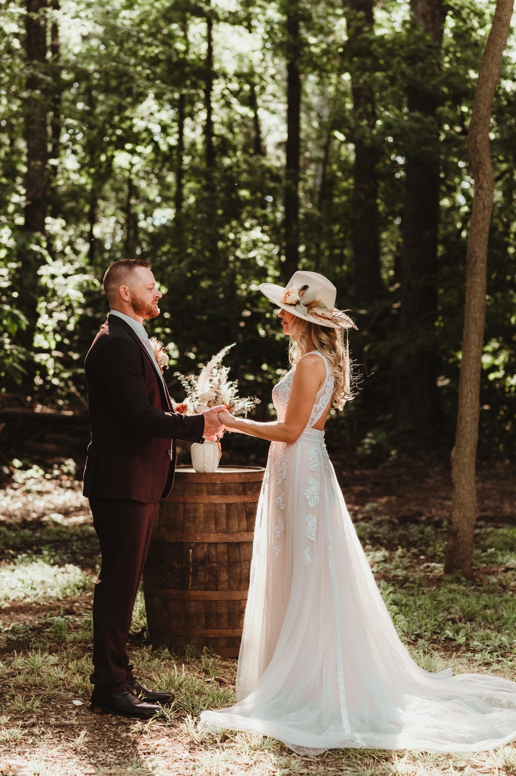 A bride and groom are standing in the woods holding hands.