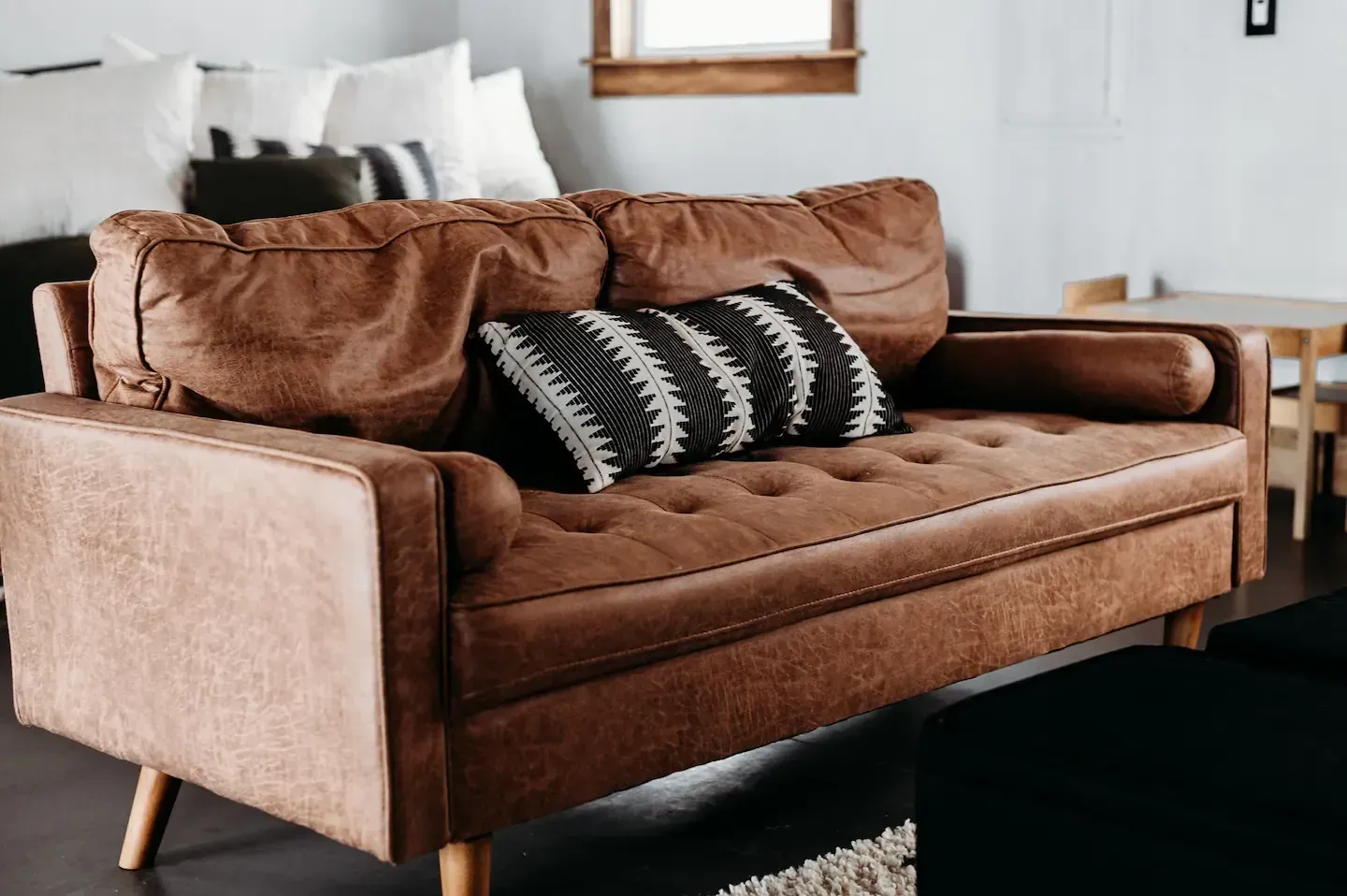 A brown leather couch with black and white pillows in a living room.