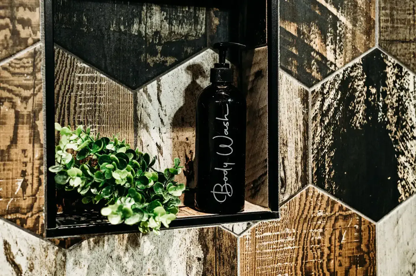 A bottle of bath wash is sitting in a niche on a tiled wall.