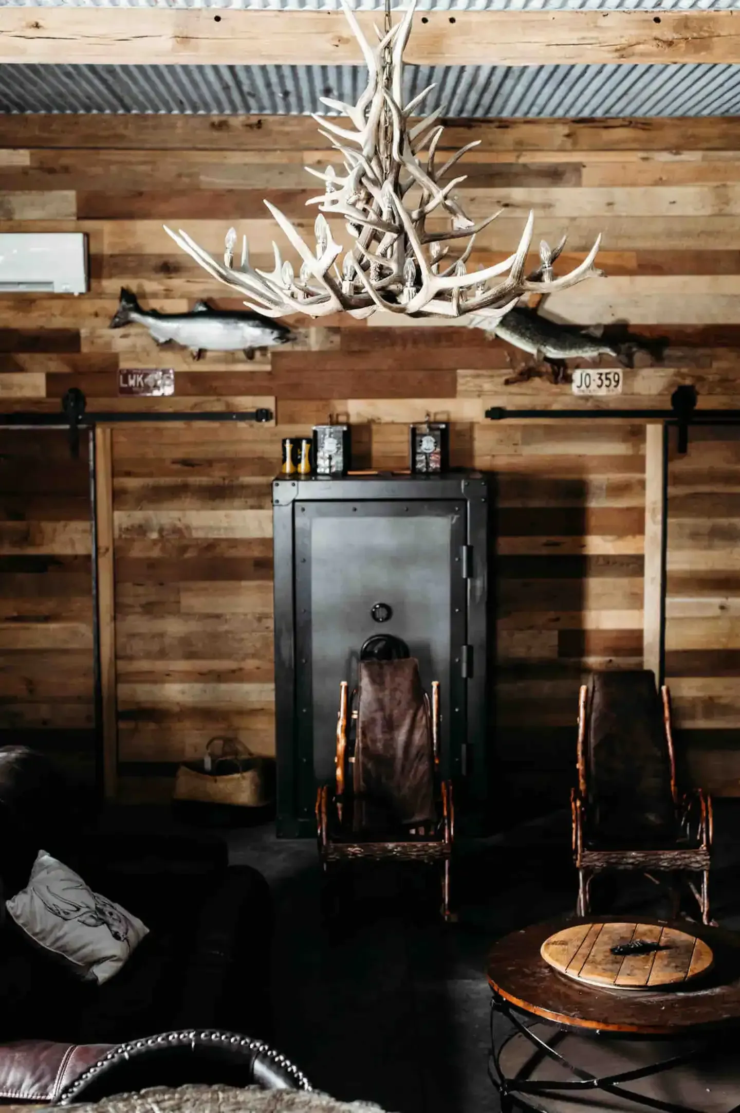 A living room with wooden walls , chairs , a table and a safe.