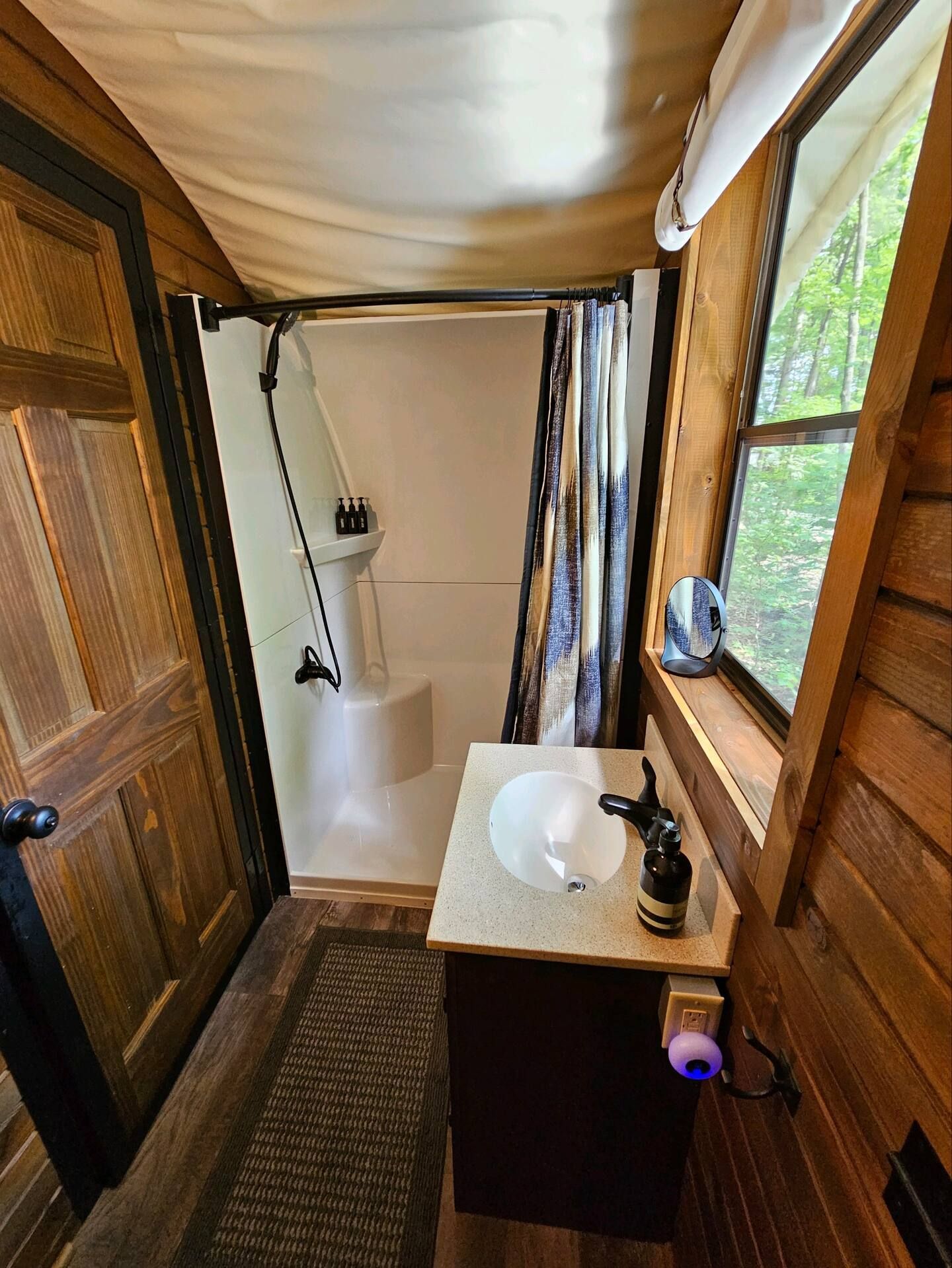 A bathroom with a sink , shower , mirror and window.