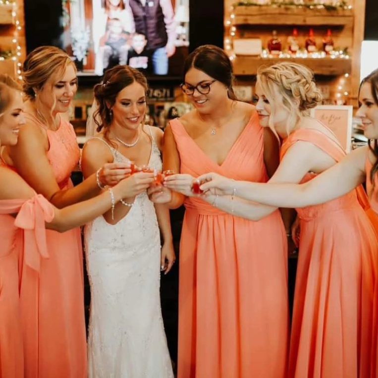 Bride and bridesmaids in coral dresses toasting drinks at a wedding reception
