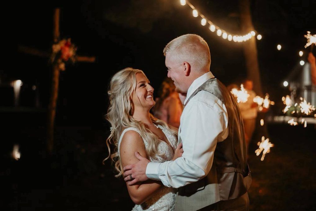 Couple dancing outdoors at night under warm string lights, smiling and holding each other
