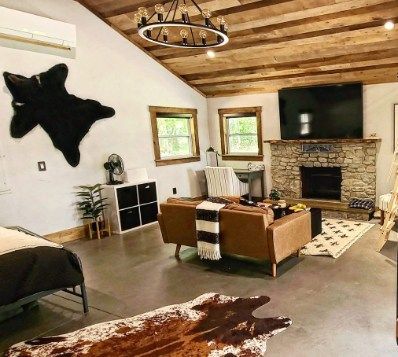 Rustic living room with stone fireplace, leather sofa, cowhide rug, and wood beam ceiling