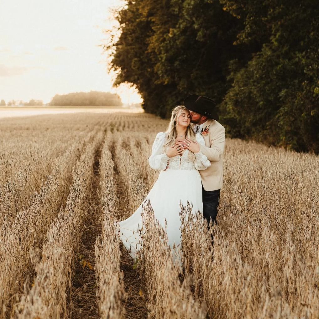 Couple embracing in a golden field at sunset, with tall trees framing the scene
